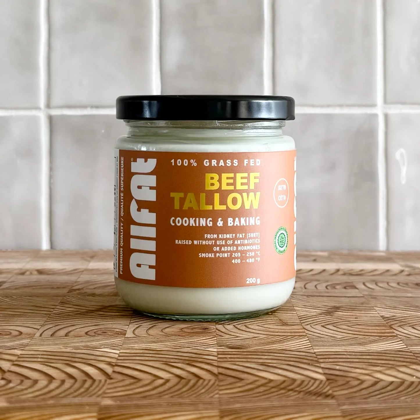 Jar of beef tallow on a wooden surface with a tiled wall background