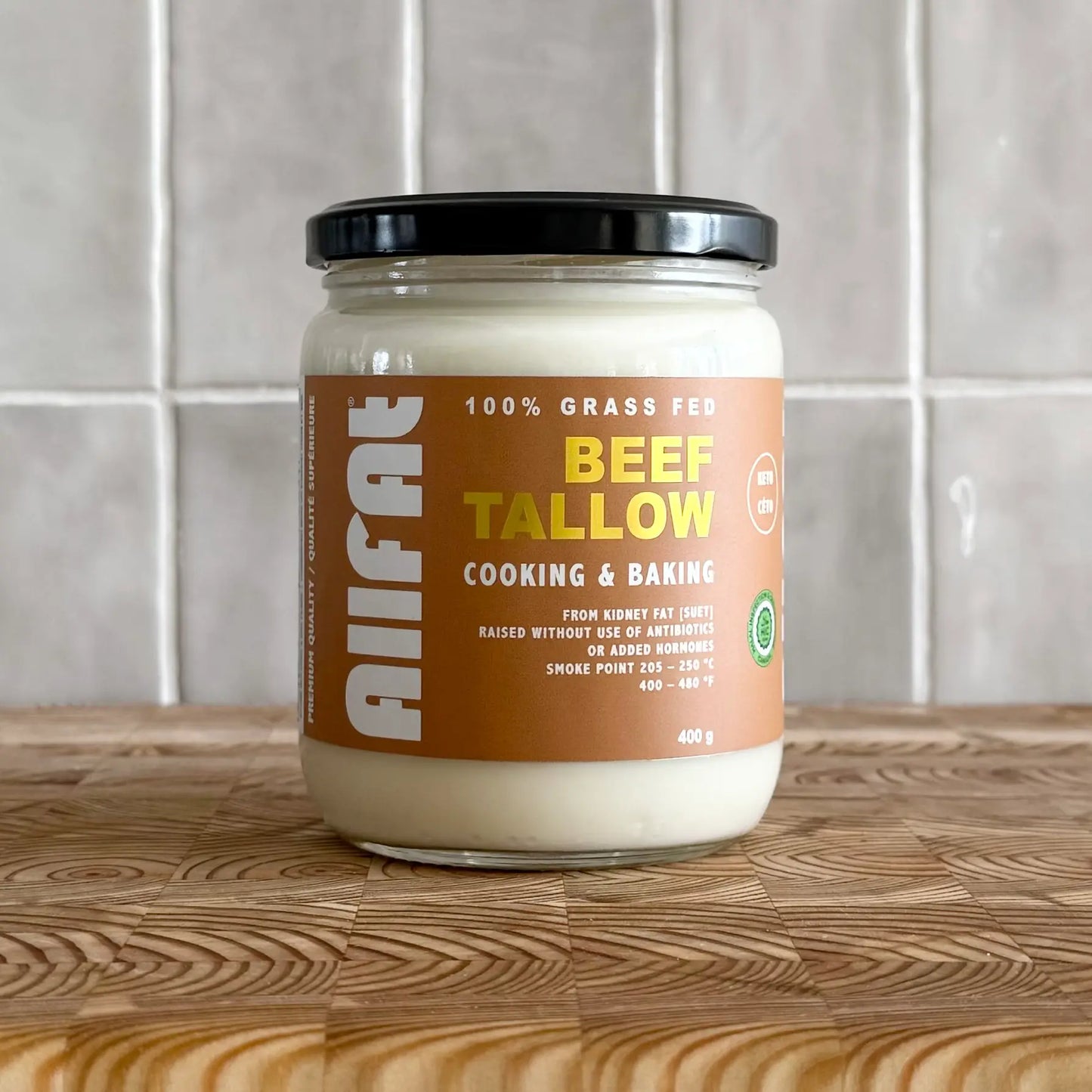 Jar of beef tallow on a wooden surface with a tiled wall background