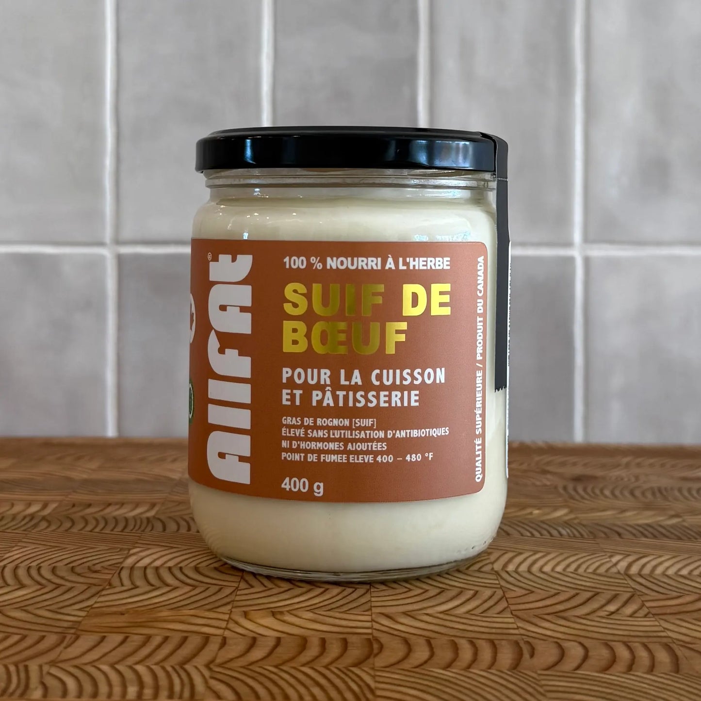 Jar of beef fat on a wooden surface with a tiled wall background