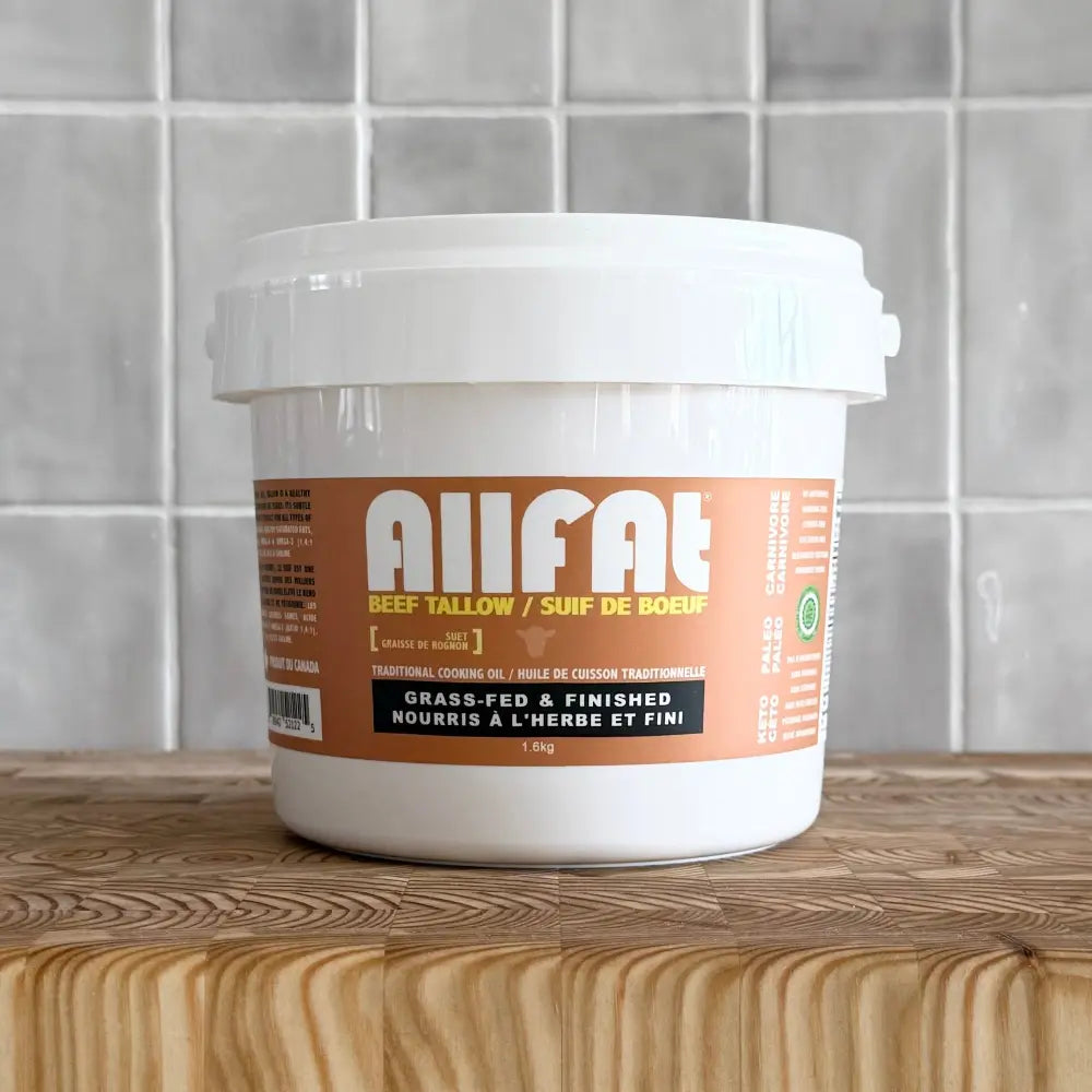 White plastic tub 1.6 kg of beef tallow allfat on a wooden cutting board against a tiled background.