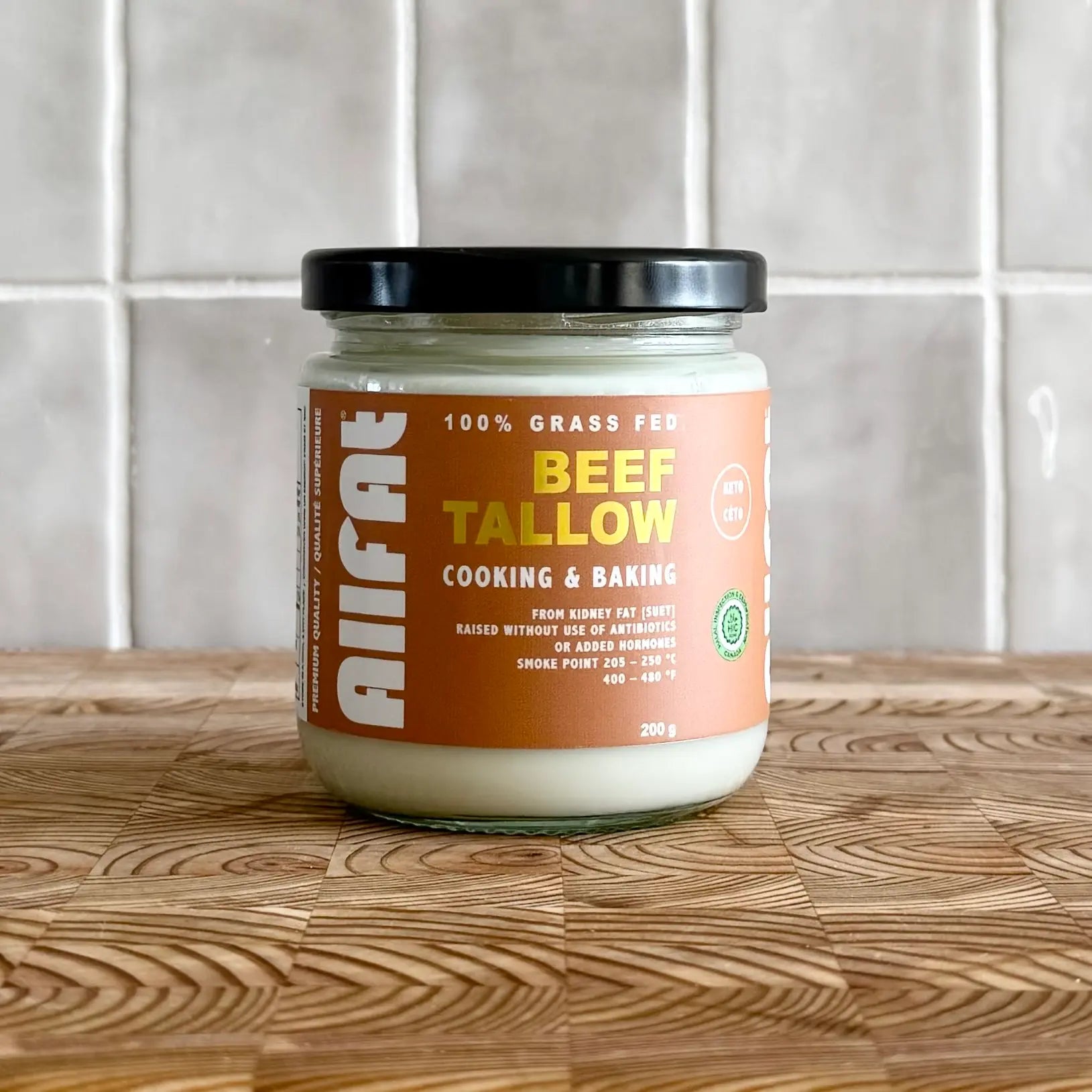 Jar of allfat canadian beef tallow on a wooden surface with a tiled wall background