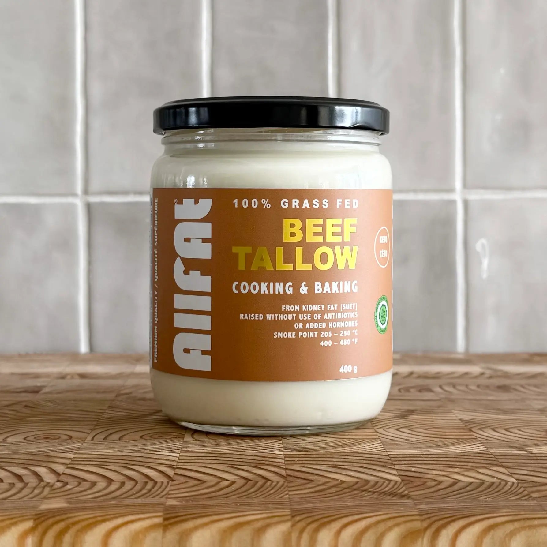 Jar of allfat canadian beef tallow on a wooden surface with a tiled wall background