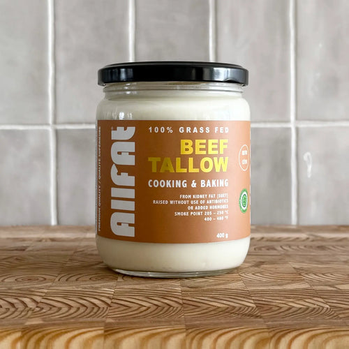 Jar of allfat canadian beef tallow on a wooden surface with a tiled wall background