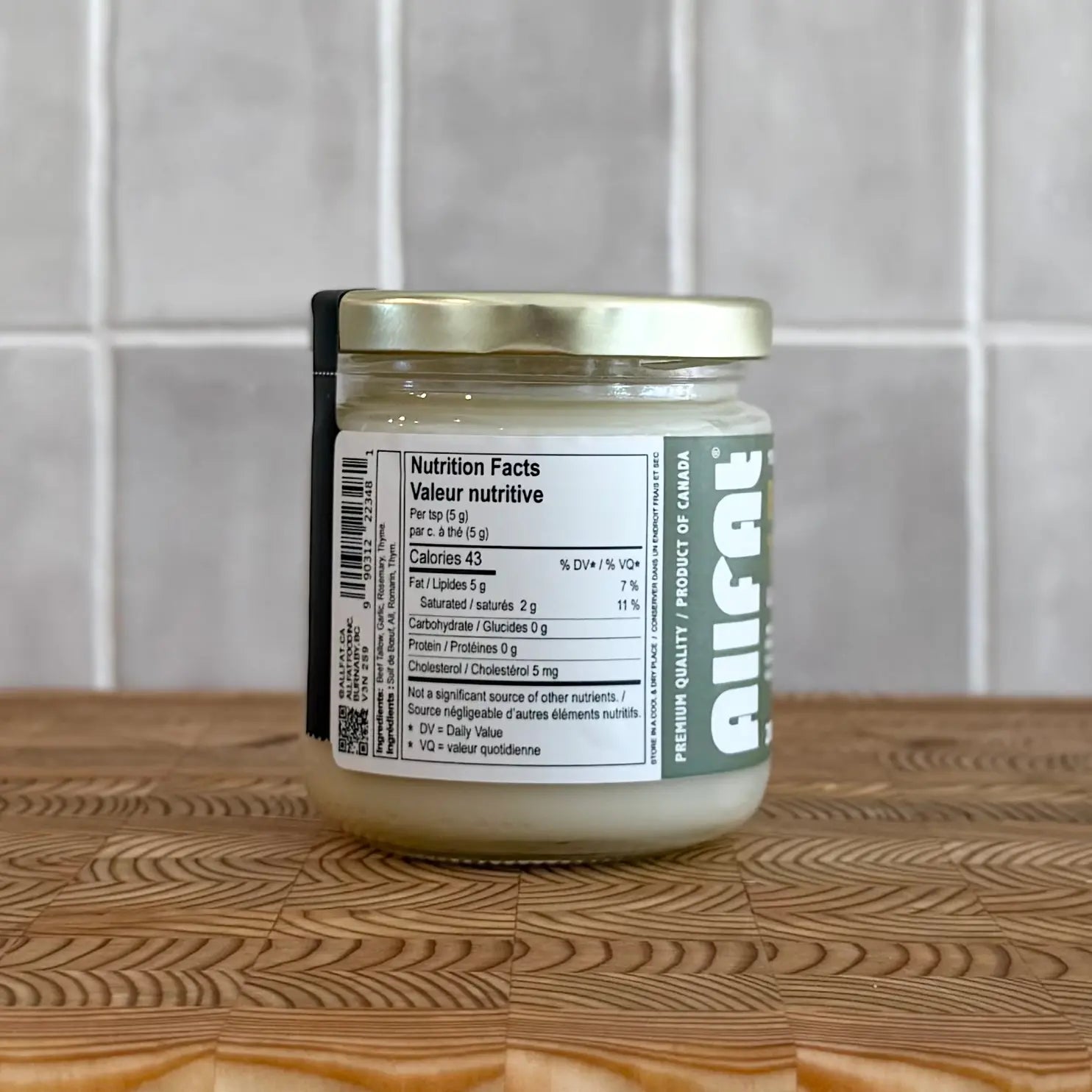 Jar of allfat beef tallow garlic rosemary on a wooden surface with a tiled wall background