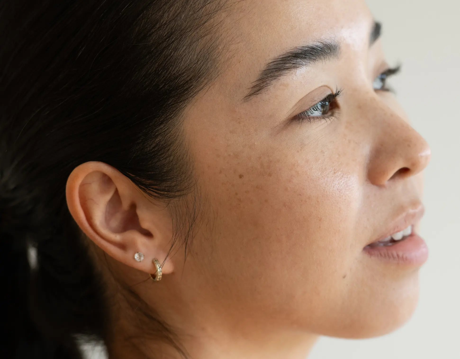 Close-up of a woman's face with a neutral expression, wearing an earring.