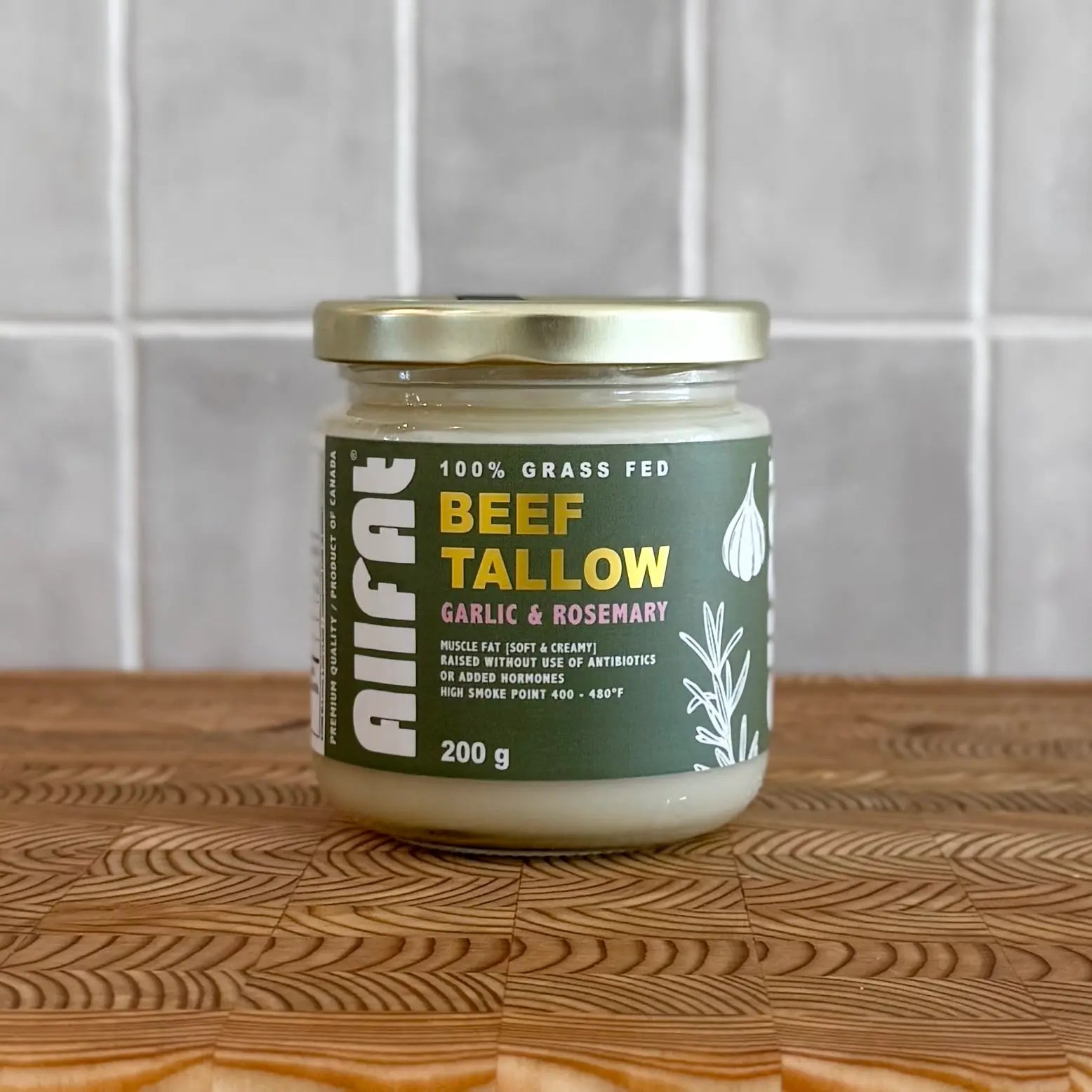 Jar of beef tallow with garlic and rosemary flavor on a wooden surface.