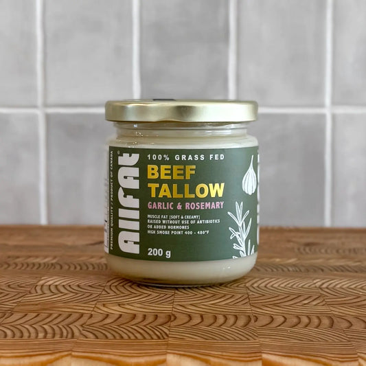 Jar of beef tallow with garlic and rosemary flavor on a wooden surface.