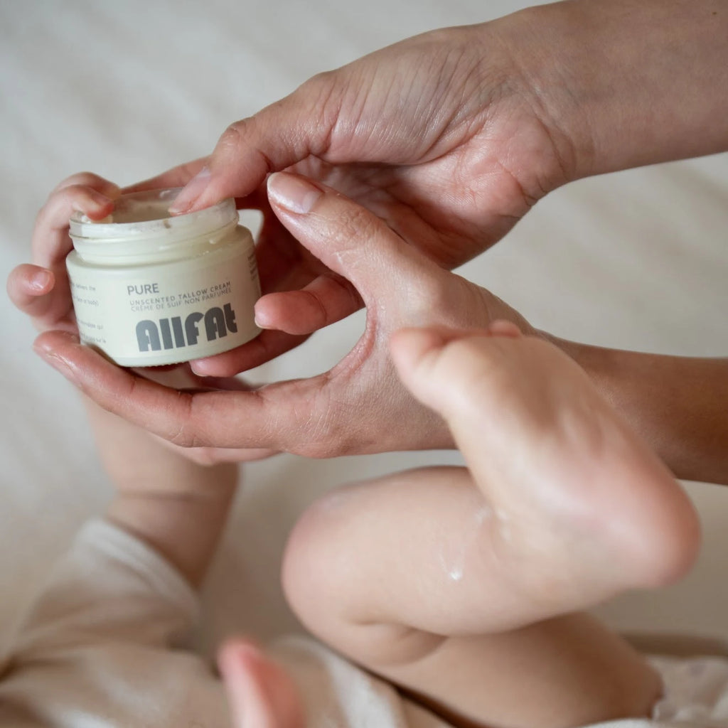 Person applying tallow cream from a jar labeled 'allfat' to their baby and hands.