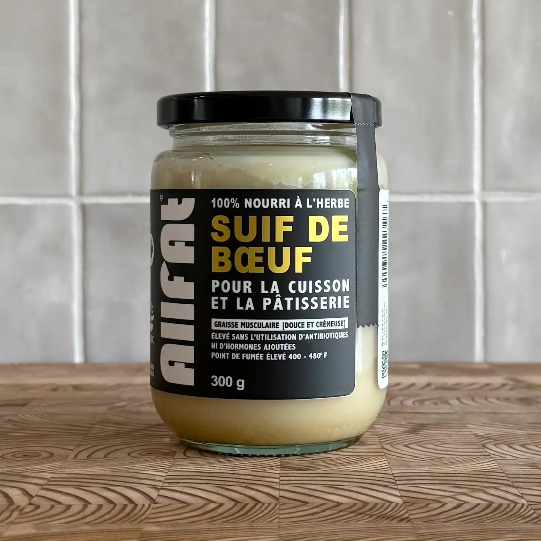 Jar of beef fat on a wooden surface with a tiled wall background