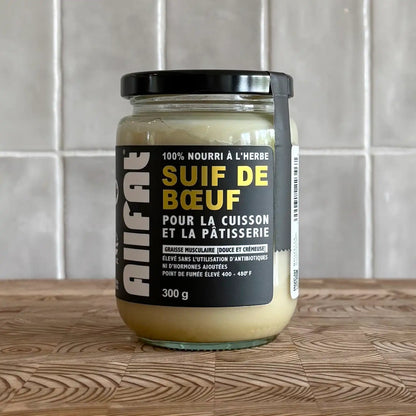 Jar of beef fat on a wooden surface with a tiled wall background