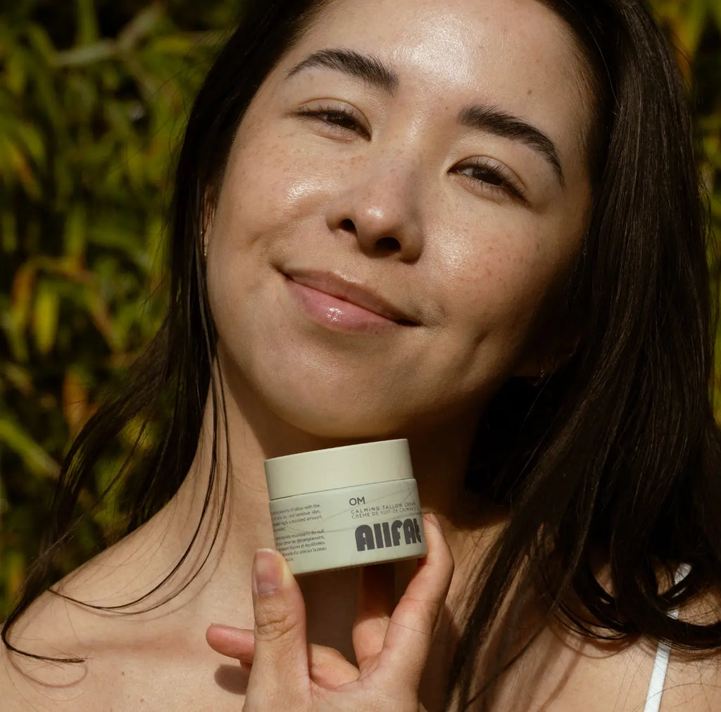 Woman holding a skincare allfat tallow cream product with a blurred natural background
