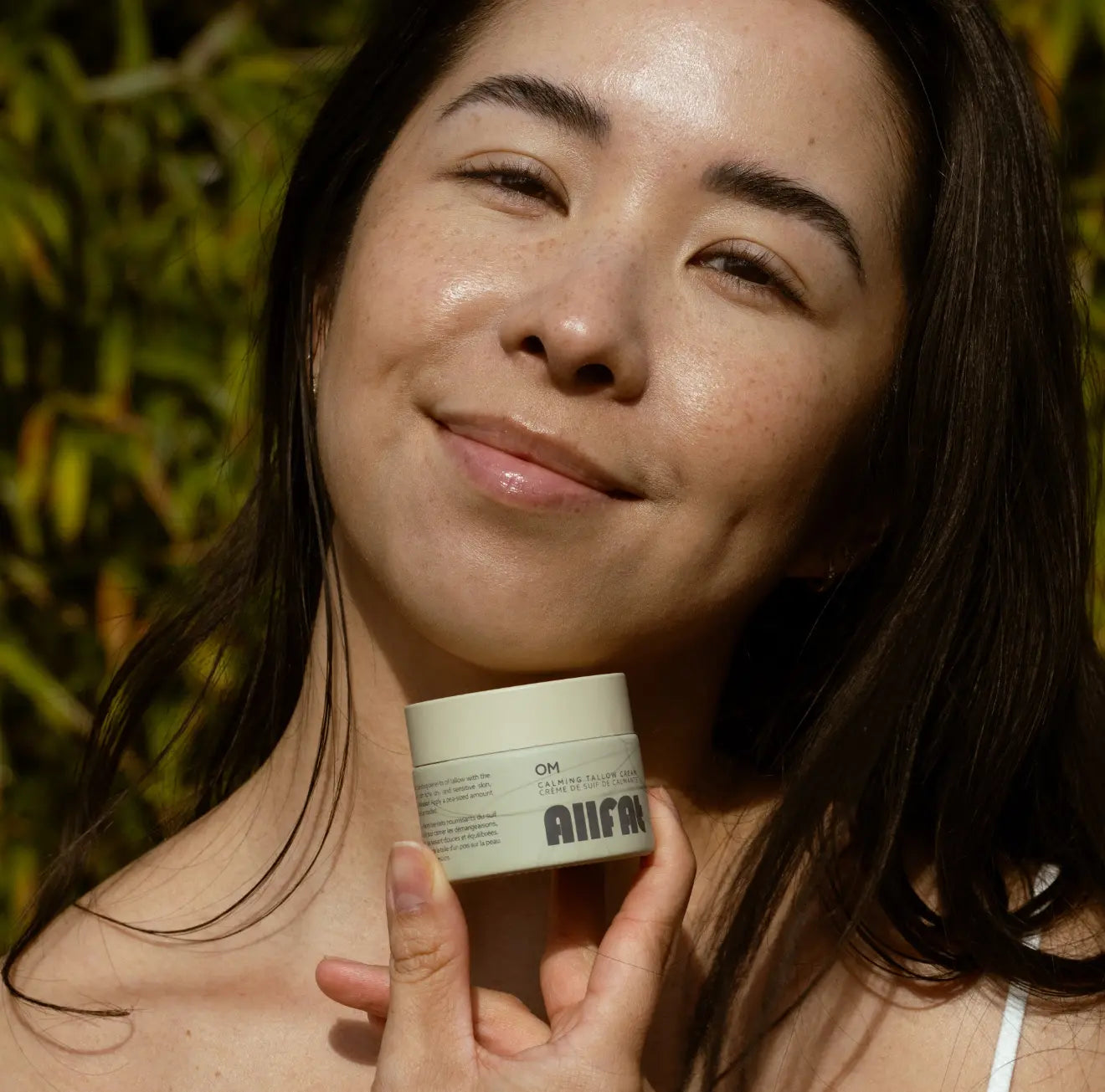 Woman holding a skincare allfat tallow cream product with a blurred natural background