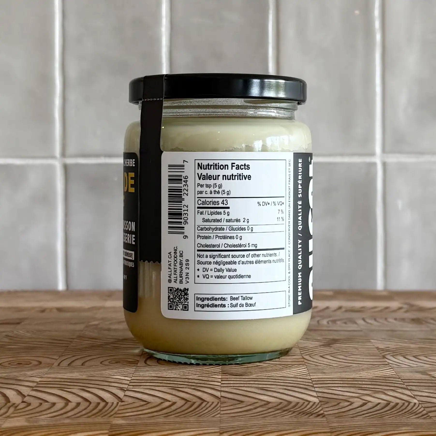 Jar of allfat canadian beef tallow for cooking with a nutrition label on a wooden surface and tiled wall background