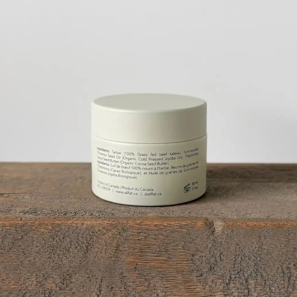 White jar of tallow cream with text on a wooden surface and light gray background