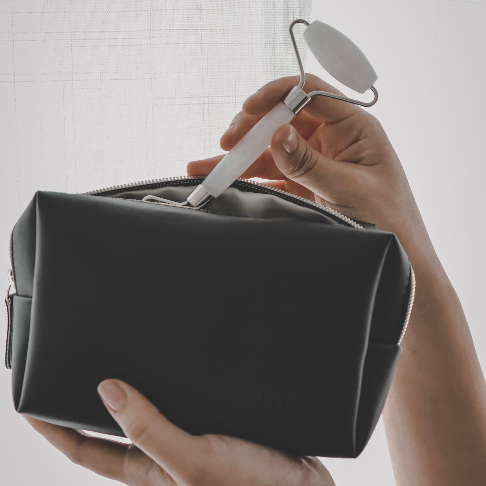 Person holding a black toiletry bag with a white roller tool inside, against a light background.