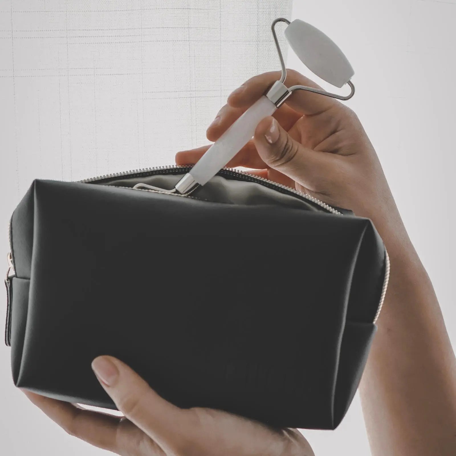 Person holding a black toiletry bag with a white makeup roller inside, against a neutral background.