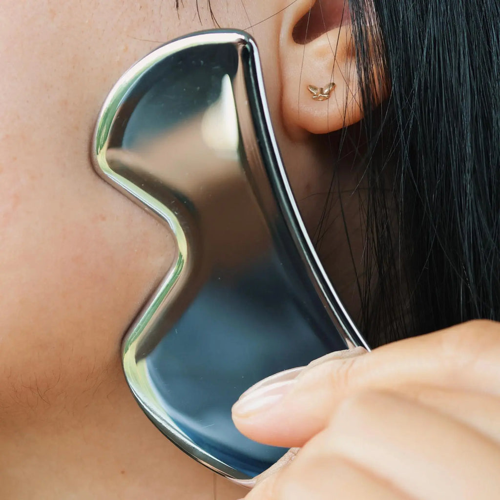 Person using a silver Gua Sha tool on their neck