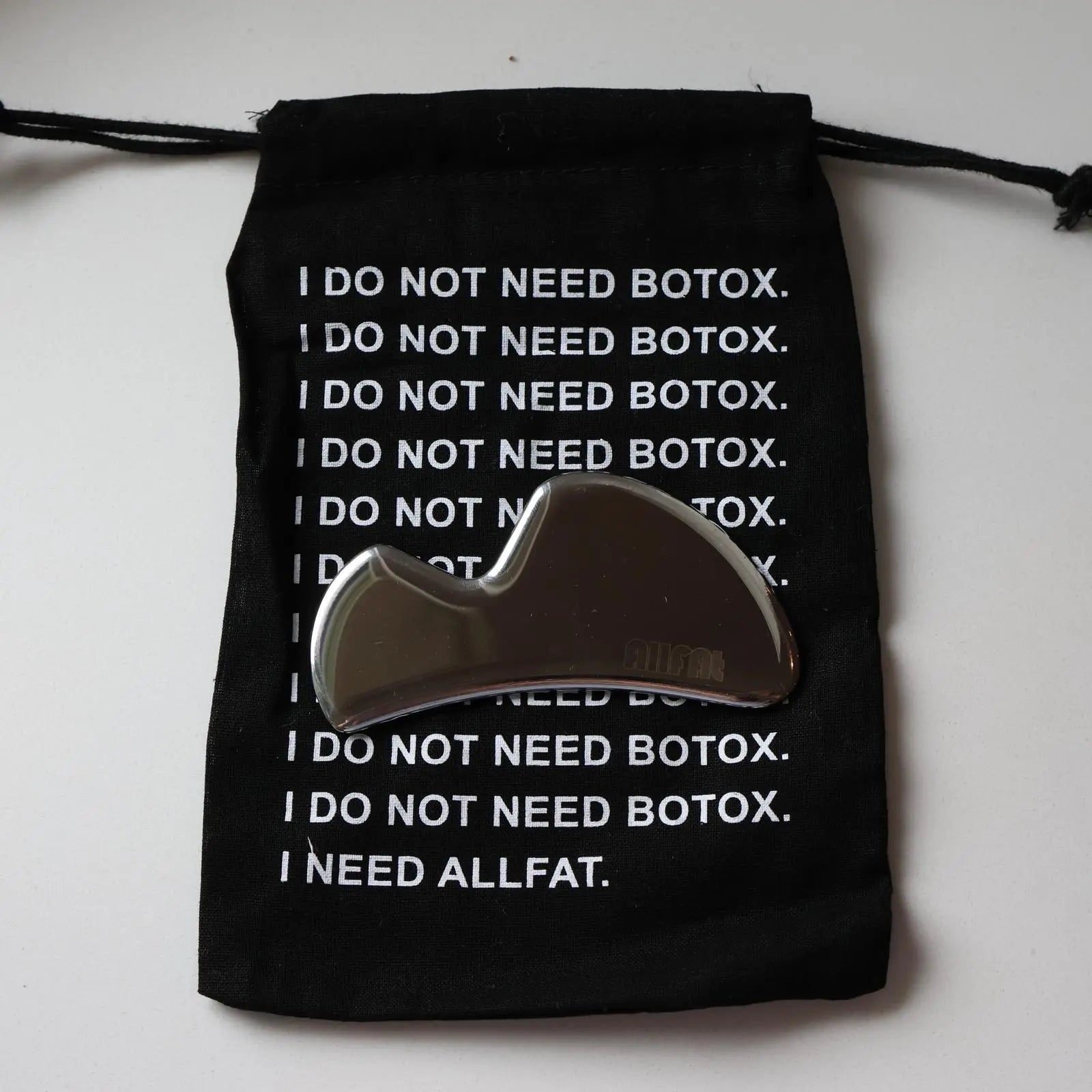 Black drawstring bag with text and a gua sha tool on a white background