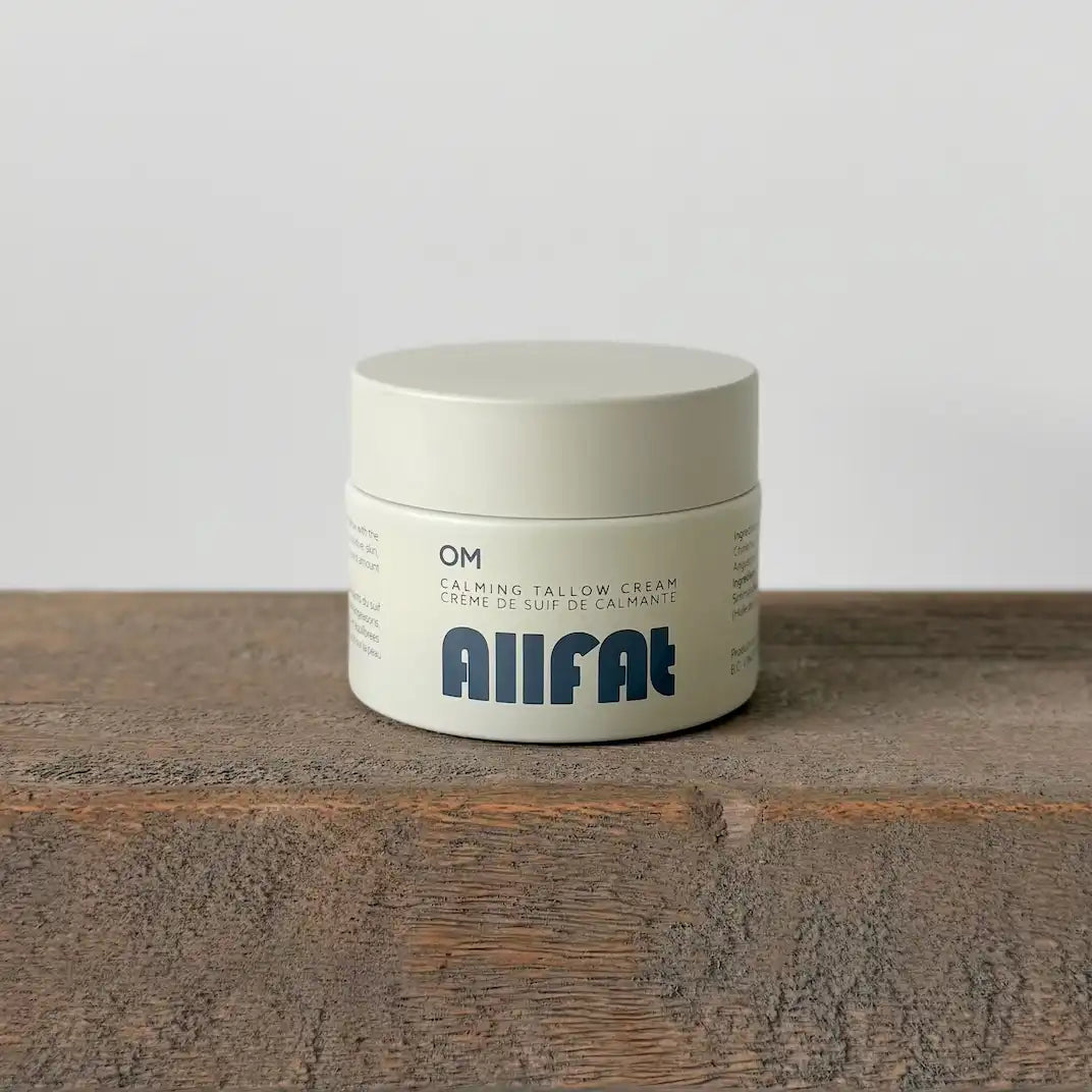 Jar of AIIFAT calming tallow cream on a wooden surface with a plain background