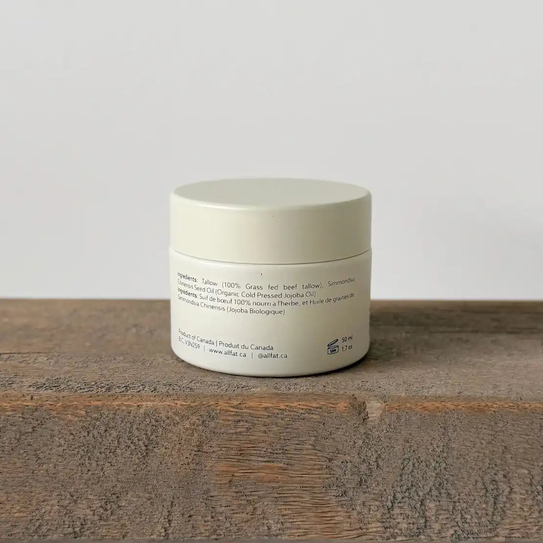White tallow cream jar with text on a wooden surface and light gray background
