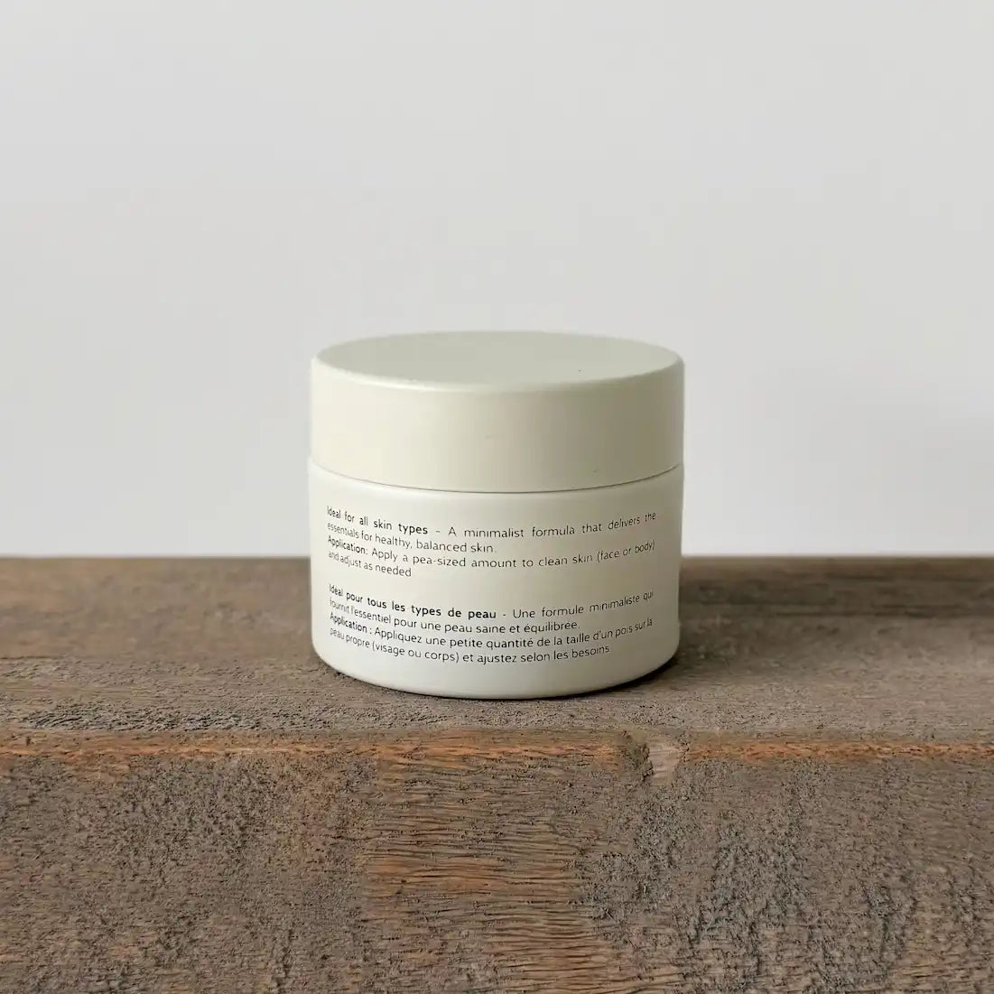 White tallow cream jar with text on a wooden surface and light gray background