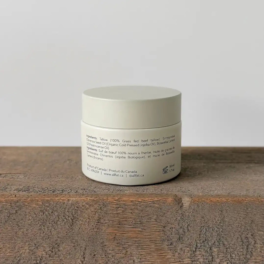 White tallow cream jar with text on a wooden surface and light gray background
