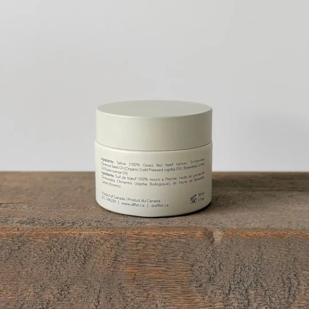 White tallow cream jar with text on a wooden surface and light gray background